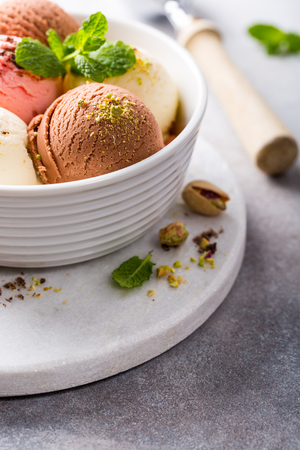 Assorted ice cream scoops of different colors and flavours in white bowl with pistachio nuts, chocolate and mint decoration. Summer food concept with copy space.の写真素材