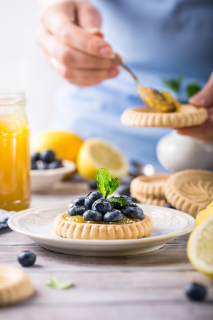 Shortbread homemade tartlet filled with lemon curd and fresh blueberries with womens hands on rustic wooden background. Holiday food concept.の写真素材