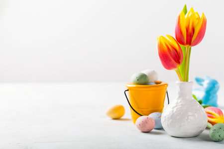 Easter composition with spring tulips flowers in white vase and colored quail eggs candies in...