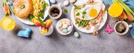 Easter breakfast flat lay with scrambled eggs bagels, orange tulips, bread toast with fried egg and green asparagus, colored quail eggs and spring holidays decorations. Top view. Copy space.の写真素材