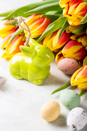 Easter greeting card with colored quail eggs candies, green ceramic rabbit and tulips flowers. Spring holidays concept with copy space.の写真素材