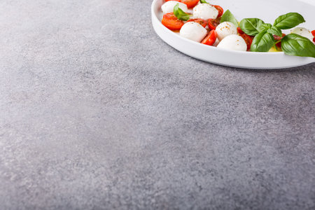 Delicious caprese salad with ripe cherry tomatoes and mini mozzarella cheese balls with fresh basil leaves. Italian healthy food concept with copy space.の写真素材