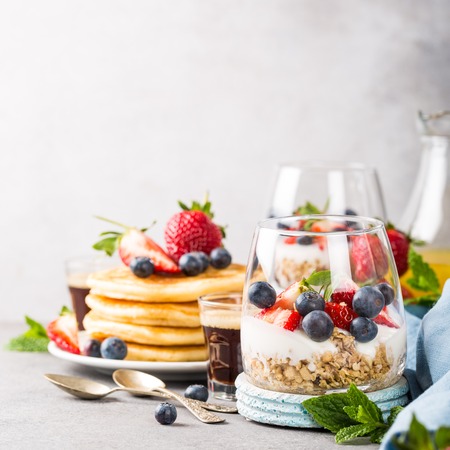 Oatmeal granola with berries and yogurt and panccakes on light gray concrete background. Healthy breakfast food concept with copy space.の写真素材