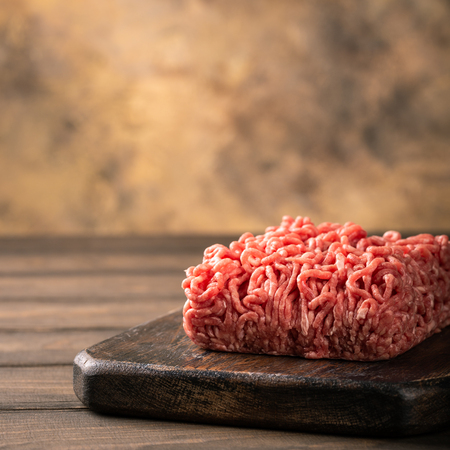 Fresh raw beef minced meat on dark wooden board. Healthy food ingredients concept with copy space.の写真素材