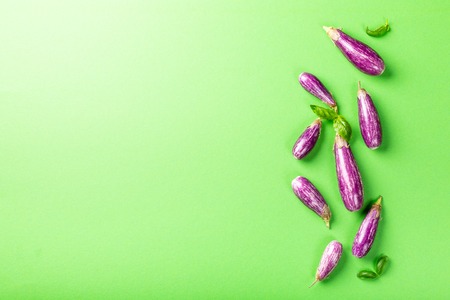 Heap of small eggplant or aubergine vegetable with basil leaves on green background. Healthy food concept with copy space.の写真素材