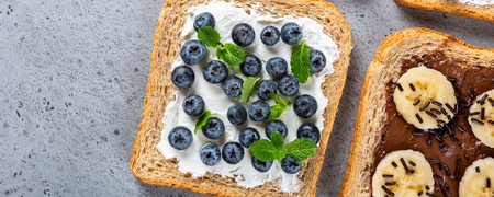 Delicious open sandwiches with goat cheese and blueberries and chocolate and banana on gray table. Breakfast background. Copy space, top view, bannerの写真素材