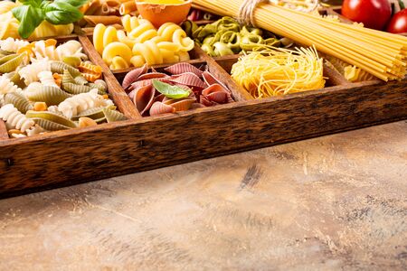 Spaghetti and assorted colorful italian pasta in wooden box. Healthy food background concept. Flat lay, top view, copy space.の写真素材