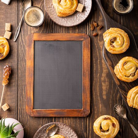 Food background with fresh pastry sweet swirl buns with raisins for breakfast or brunch and coffee, with black chalkboard. Top view, copy space.の写真素材