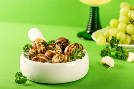 French cuisine Bourgogne Escargot Snails with garlic herbs butter in ceramics pan on green background with copy spaceの写真素材