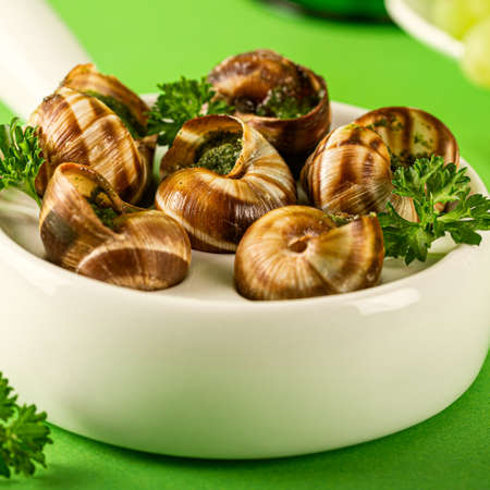 Baked Bourgogne Escargot Snails with garlic herbs butter in ceramics pan on green background, close upの写真素材