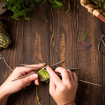 Flat lay with knitting green socks in progress with female hands. Cozy homely atmosphere with wooden...