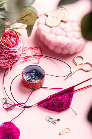 Vibrant yarn and knitting tools are beautifully arranged on a pink surface, highlighting textures...