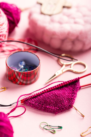 Knitting socks project features bright pink yarn, scissors, and stitch markers on a soft pink surface, highlighting the joy of crafting and the creative processの写真素材