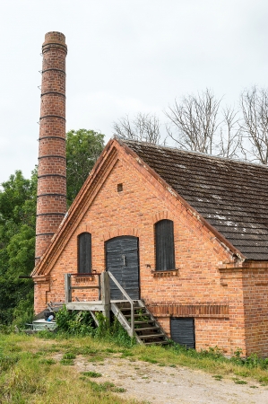 Old abandoned brick factory with chimney and wooden stairs on outside. の写真素材