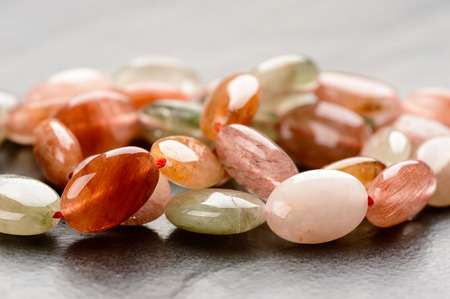 A strand of colorful rutile quartz beads on red string resting on black stone plate.の写真素材