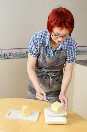 Adult woman cutting and weighing butter on kitchen table at home.の写真素材