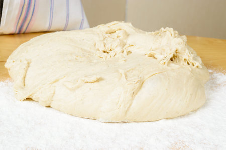 Lump of bread dough on wheat flour on wooden table.