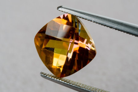 Topaz gemstone in cushion cut held by tweezers.