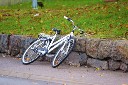 White bicycle resting against granite boulders beside walkway. Green grass in background and street in foreground.のeditorial素材