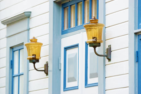Antique golden lighting with metal arms outside white and blue building, on either side of door. Seen from side with one light in focus and the other out of focus.のeditorial素材