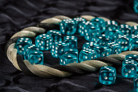 Lots of blue transparent plastic dices on black fabric. Twined silver metal necklace framing dices.