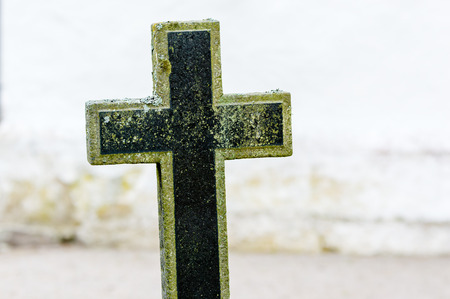 Christian black cross on grave yard.White church wall out of focus in background.の写真素材