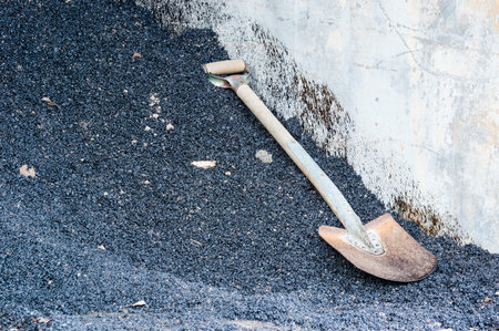 One spade on pile of tarmac or oil gravel. Concrete wall beside spade with oil staines on.の写真素材