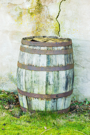 Old and weathered wooden barrel against concrete wall with cracks.の写真素材