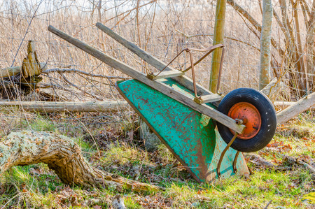 Upside down wheelbarrow leaning against net fence in early spring.の写真素材