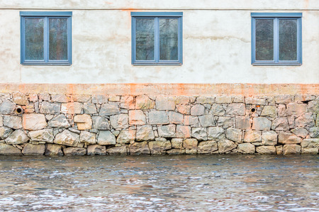 Three blue windows and three vertical levels of beige, orange and water. Outside of industrial building facing a river.の写真素材