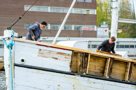 Karlshamn Sweden  May 06 2015: Two unknown workers renovate an old fishing boat in the harbor of Karlshamn. Persons work hard and boat is stripped of wood.のeditorial素材