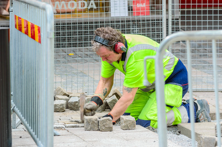 Karlshamn Sweden  May 06 2015: Unknown male paver at work with setting granite stones in public street. He is working within a fenced area outside shops.のeditorial素材