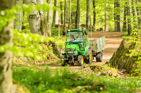 RONNEBY, SWEDEN - May 11, 2015: Small John Deere compact utility tractor 2520 used in the forest on narrow path. Here seen with a trailer in surrounding beech forest.のeditorial素材