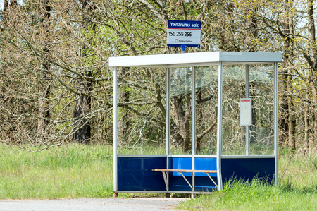 Yxnarum, Sweden - May 11, 2015: Empty bus stop shelter with small bench. Forest in background and high grass at sides. Sign on top of shelter with bus numbers and place name.のeditorial素材