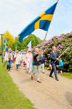 Ronneby, Sweden - June 06, 2015: People march with flags to celebrate the Swedish National day in public park. Rhododendron in bloom in background.のeditorial素材