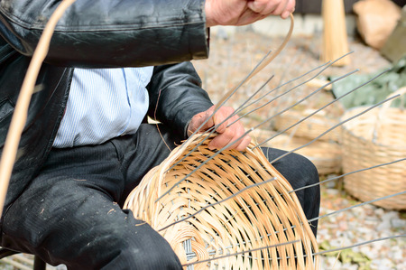 Unknown person making a wooden basket by hand. The wood is weaved into steel wires. Person is sitting down while working.の写真素材