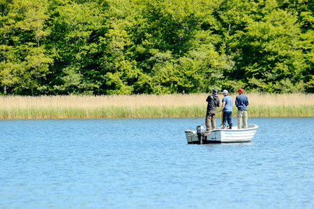 Almo, Sweden - June 11, 2015: Friends out fishing with rods in a boat near the coastline one fine summer day.のeditorial素材