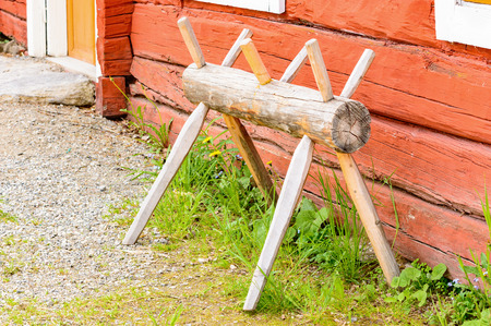 Old antique sawhorse in traditional style outside a red farm house.の写真素材