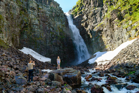 Njupeskar, Sweden â July 01, 2015: Young male scout taking picture of a young female scout in front of waterfall. Njupeskar is Swedens tallest waterfall with a total height of about 93 meters.のeditorial素材
