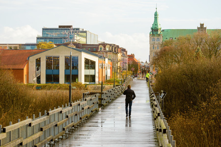 Kristianstad, Sweden - November 12, 2015: The Naturum bridge connects the Vattenriket biosphere and nature reserve with the city center across a river. Here is a man walking on the wet bridge to town.のeditorial素材