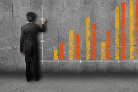 businessman in suite drawing a giant bar diagram on a stone wallの写真素材