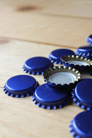 Side on view of blue beer bottle tops on a rustic wooden table. Selective focus with copyspace. Home...