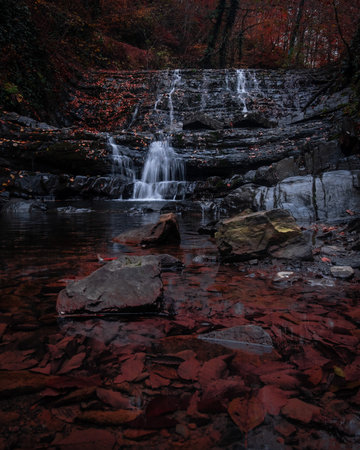 Beautiful mystic waterfalls in autumn season. View on the stream around the stones. Colorful cascade of water and red leaves around.の写真素材