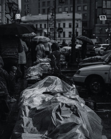 Black and white photo of a street market under the rain. People under the umbrellas in the background. Street photography concept, wet goods on market.の写真素材