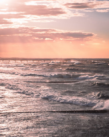 Beautiful pastel sunset with view on the pier and sea waves. Pink sky and dramatic water waves. Relaxing landscape. Photo of Baltic sea.の写真素材