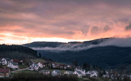 Beautiful view of the sunset in a small town in the Germany. Big mountains on the background. Fog and clouds hiding peak of the mountain. Schwarzwald natureの写真素材