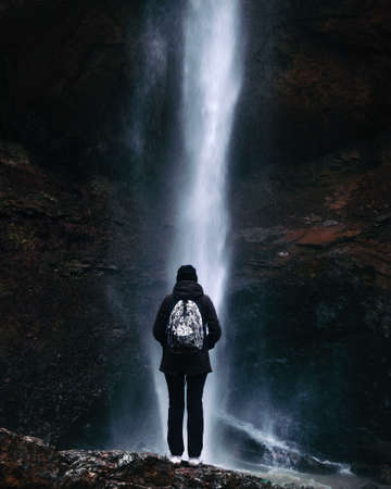 Beautiful mystic waterfall in autumn season. View on the stream falling down the cliff. Colorful cascade of water and person standing and watching at itの写真素材