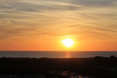 A beautiful scenery of the red horizon and cloudy sky captured during the sunsetの写真素材
