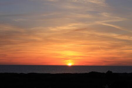 A beautiful scenery of the red horizon and cloudy sky captured during the sunsetの写真素材