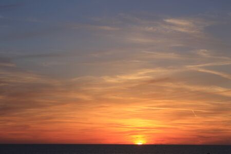 A beautiful scenery of the red horizon and cloudy sky captured during the sunsetの写真素材